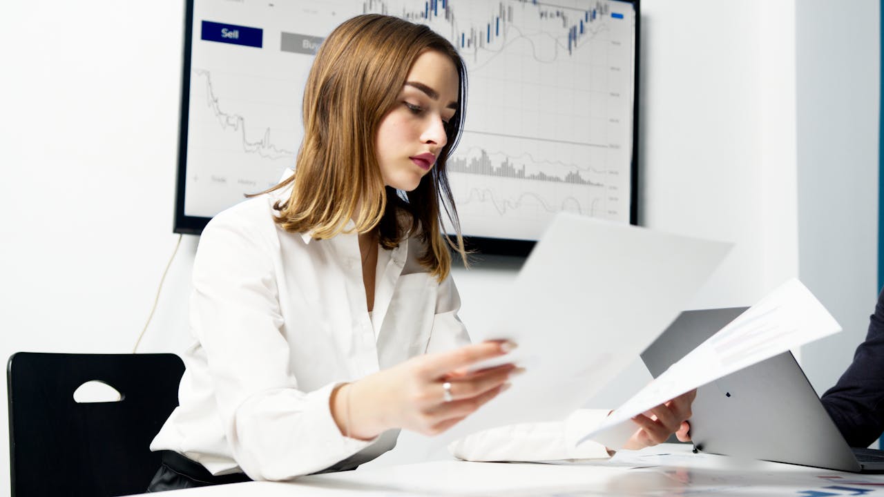 Businesswoman analyzing documents with sales data charts in background – CRM vs manual tracking concept